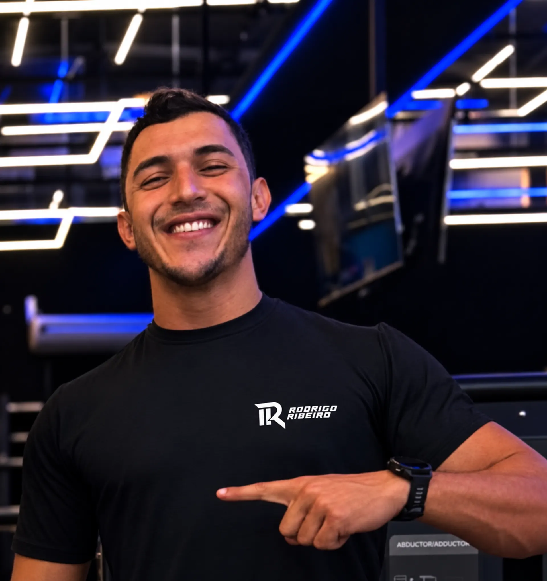 Rodrigo Ribeiro sorrindo na academia, com sua marca branca na camiseta preta